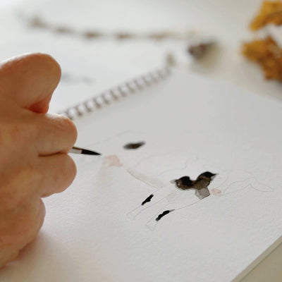 Hand holding a pen over a drawing of a face on a notebook