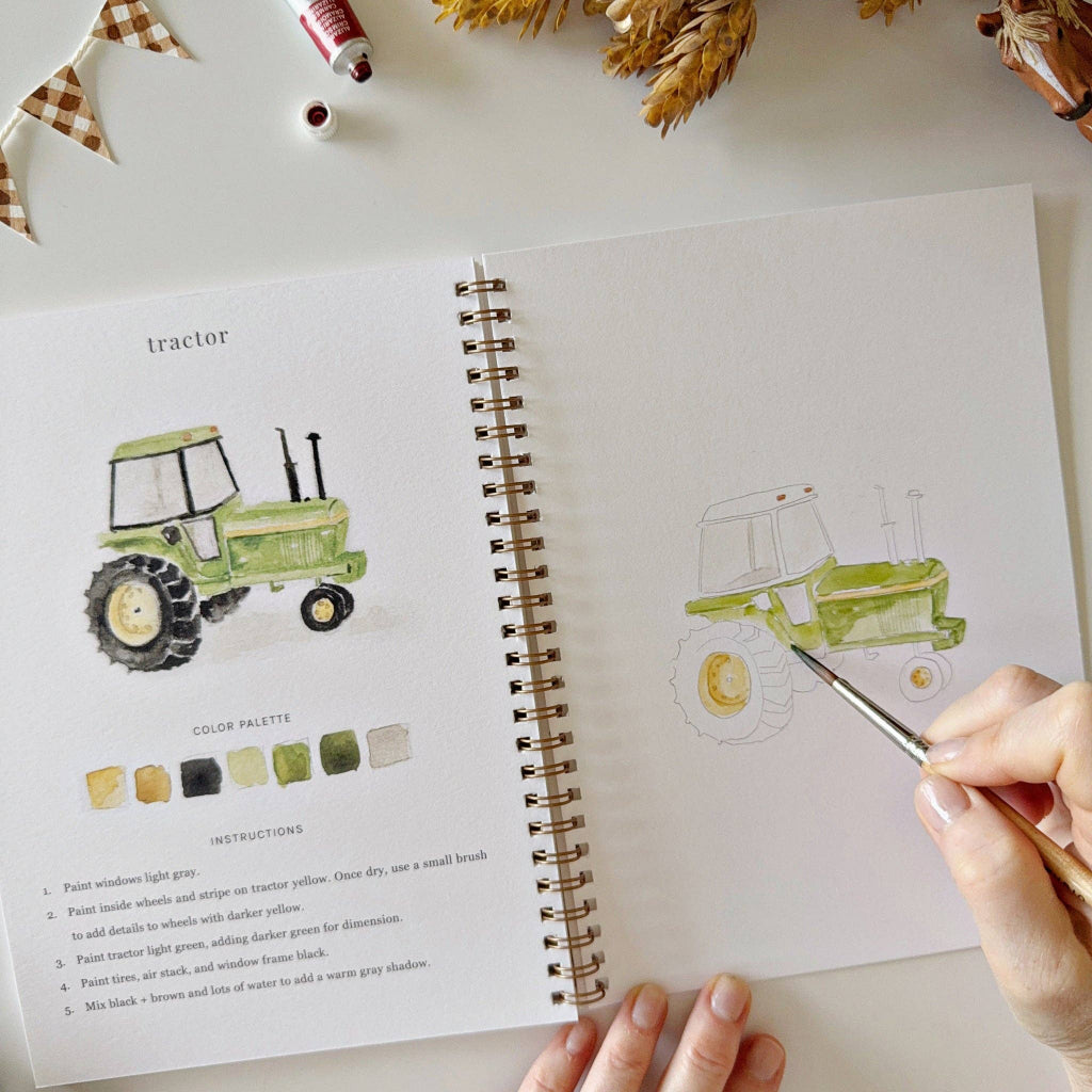 Open book with tractor illustration and color palette on a table with decorative items.