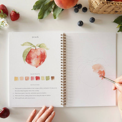 Open book with a peach illustration and color palette on a table with fruits and berries.
