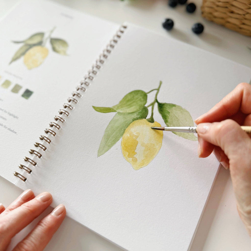 Person painting lemons with a brush on a notebook page