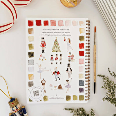 Notebook with watercolor illustrations and paint swatches on a white surface with decorative items.