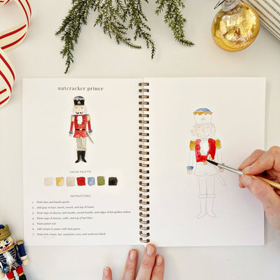 Open book with a nutcracker illustration and color chart, surrounded by Christmas decorations.
