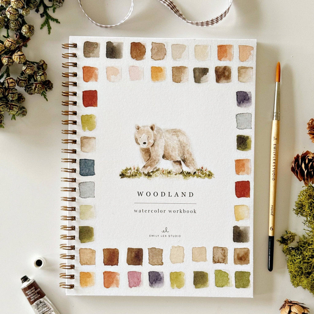 Notebook with bear illustration and 'Woodland' text on a white surface with decorative items.