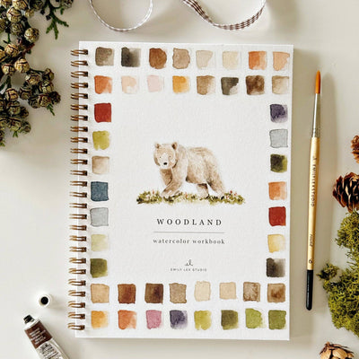Notebook with bear illustration and 'Woodland' text on a white surface with decorative items.