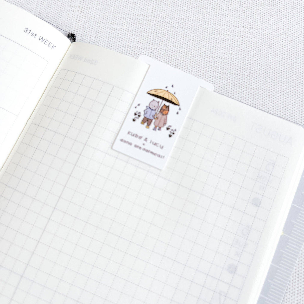 Notebook page with a bookmark of two cats under an umbrella on a white background