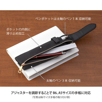 Black pen holder with a pen on a wooden surface, showing text in Japanese.