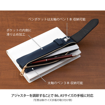 Pen case with adjustable strap on a notebook, placed on a wooden surface.