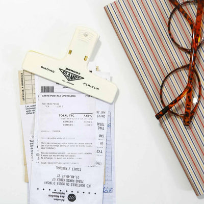 Receipt, glasses, and stationery items on a white surface with a striped notebook.