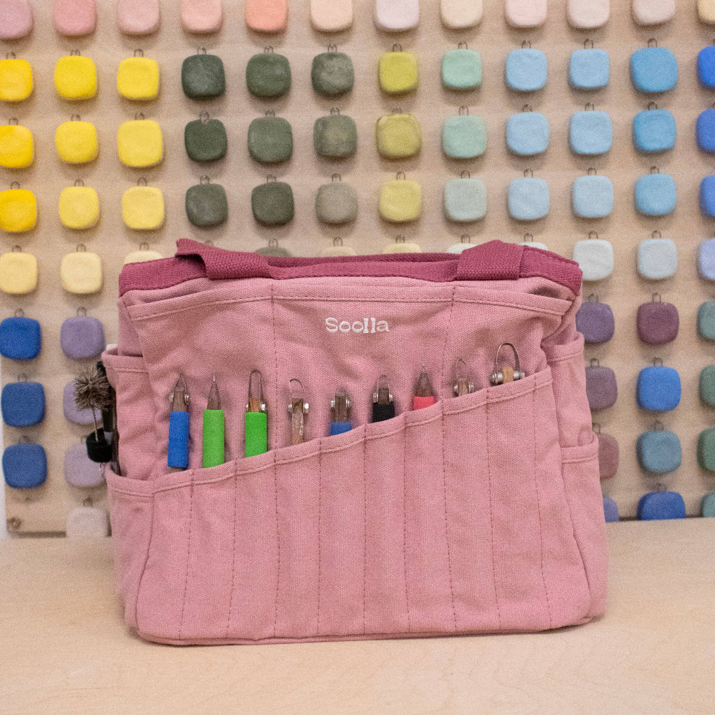 Pink tool bag with colorful tools against a multicolored square patterned wall.