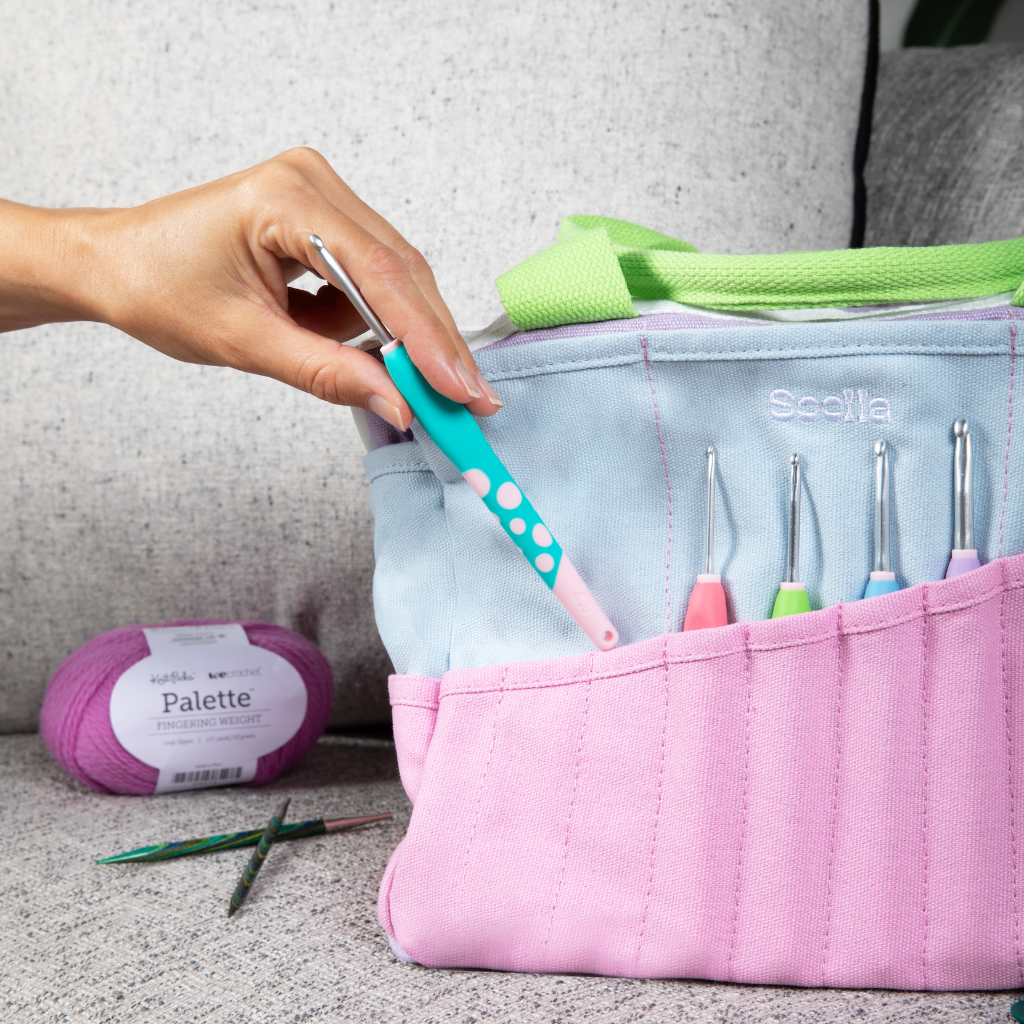 Pink Scudia crochet hook case with various hooks, yarn, and a hand holding a teal hook.