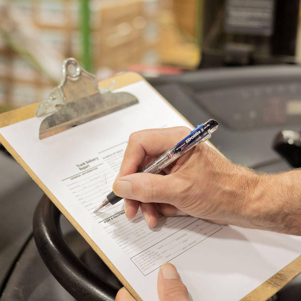 Hand holding a Tombow Reporter 3 multicolor pen over a clipboard with a form, blurred background