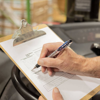 Hand holding a Tombow Reporter 3 multicolor pen over a clipboard with a form, blurred background