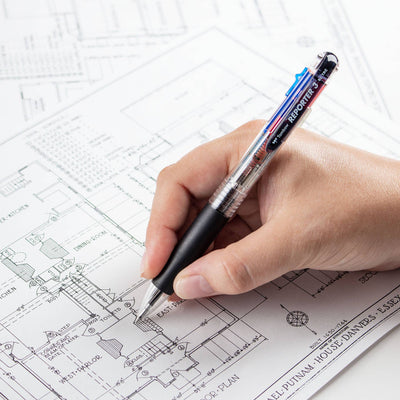 Hand holding a Tombow Reporter 3 multicolor pen over architectural blueprints