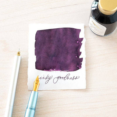 Tom's Studio Damson Ink swatch on paper with a fountain pen and ink bottle on a light wooden surface
