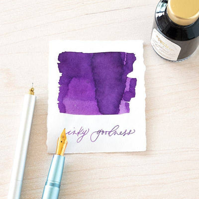 Ink swatch on paper with a fountain pen and ink bottle on a light wooden surface