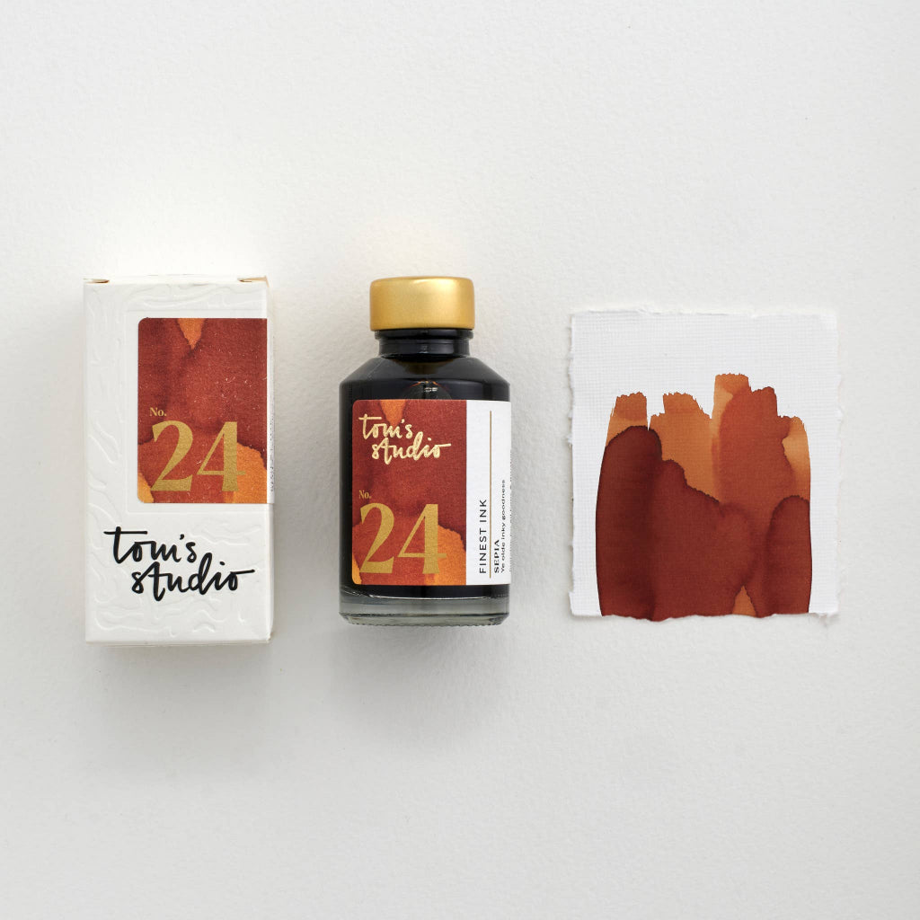 Bottle of Tom's Studio ink with packaging and watercolor swatch on a white background