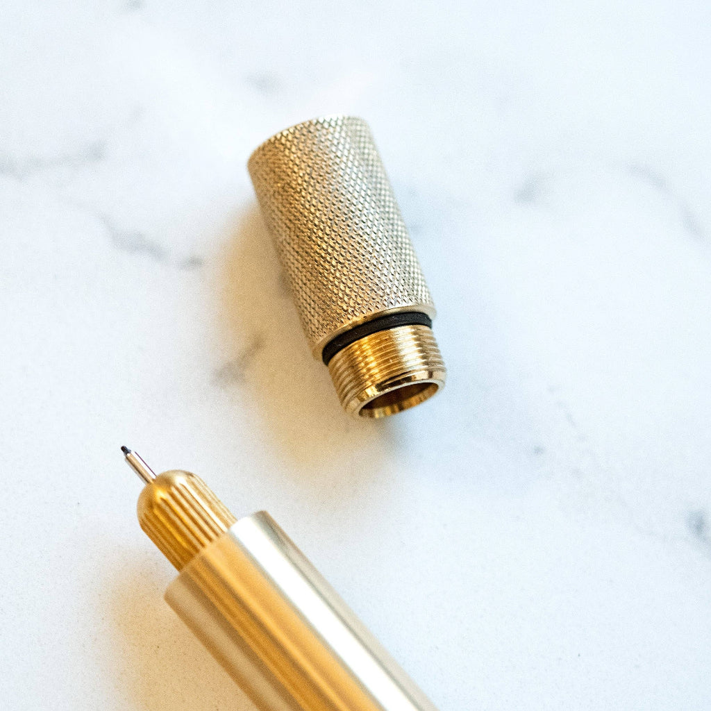Gold pen with textured cap on a marble surface