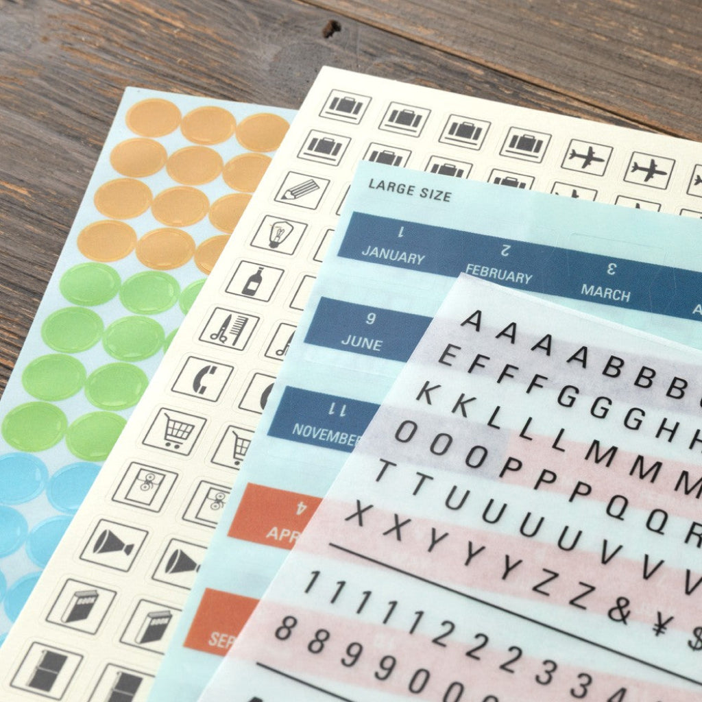 Collection of planner stickers including numbers, letters, and icons on a wooden surface.