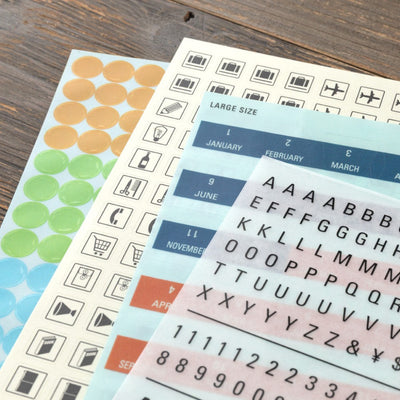 Collection of planner stickers including numbers, letters, and icons on a wooden surface.