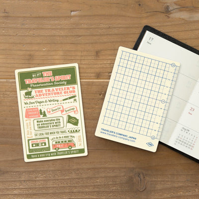 Traveler's Company notebook with grid page and promotional flyer on a wooden surface
