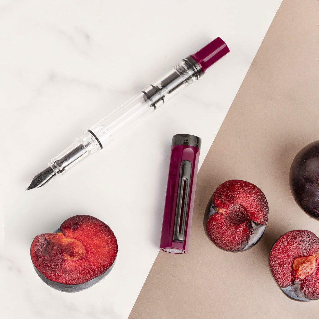 Fountain pen with plum halves on a two-tone background